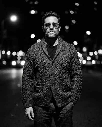 High-contrast B&W menswear editorial, chunky knit cardigan with translucent sunglasses, razor-sharp shadows, bright bokeh orbs behind
