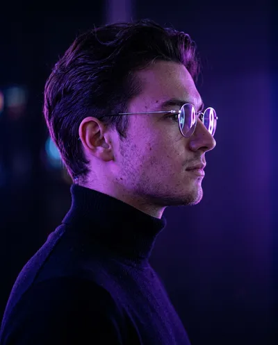 Minimalist side-profile portrait of a man in wire-frame glasses and black turtleneck, deep violet neon light sculpting his features