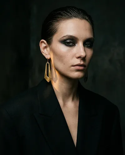 Vertical editorial close-up of a female model in a matte black oversized blazer with wide structured shoulders and a deep...