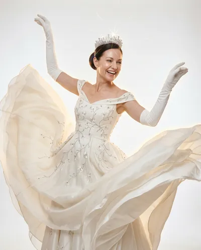 Joyful ballroom dance editorial with ivory gown billowing dramatically, crystal tiara scattering prismatic light, luminous white backdrop