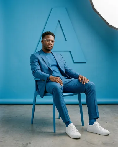 A minimalist fashion studio photoshoot featuring a stylish individual sitting with confident ease on a sleek modern chair, rendered in...