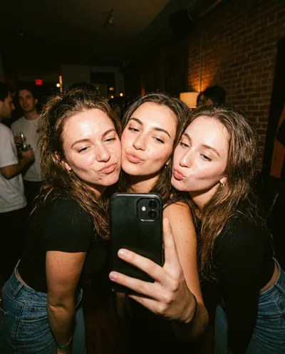 Three friends in tight party selfie with pout faces, harsh vintage flash, warm orange tone, raw authentic nightlife energy